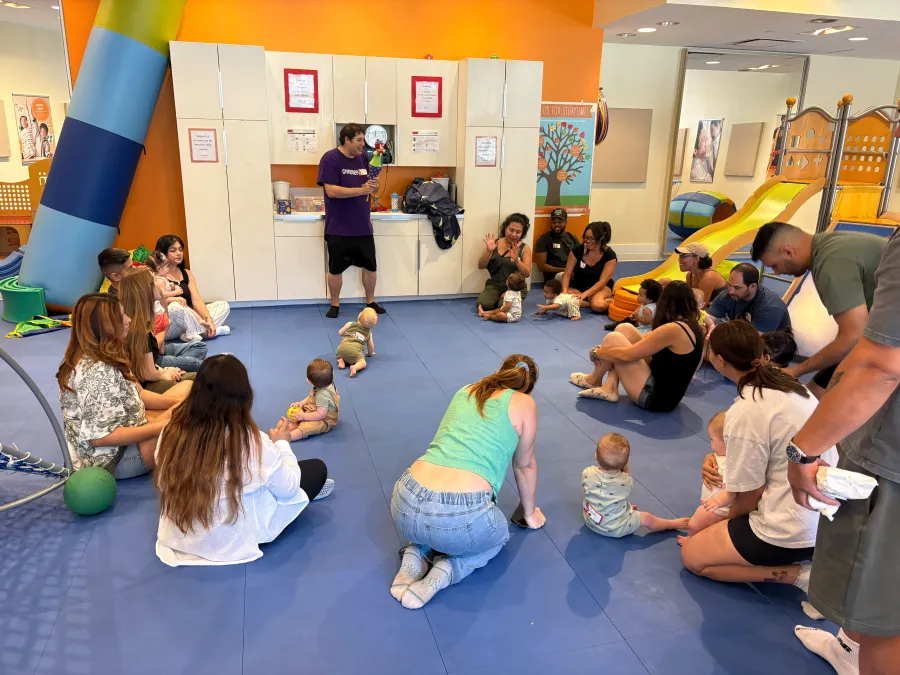 Moms, partners, and babies sitting together in a large circle at an indoor play-space meetup